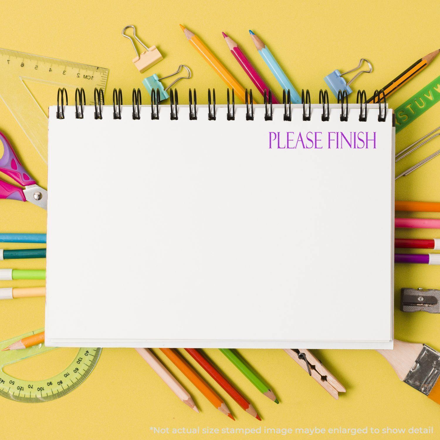 A Large Please Finish Rubber Stamp is used on a blank notebook page surrounded by colorful stationery on a yellow background.