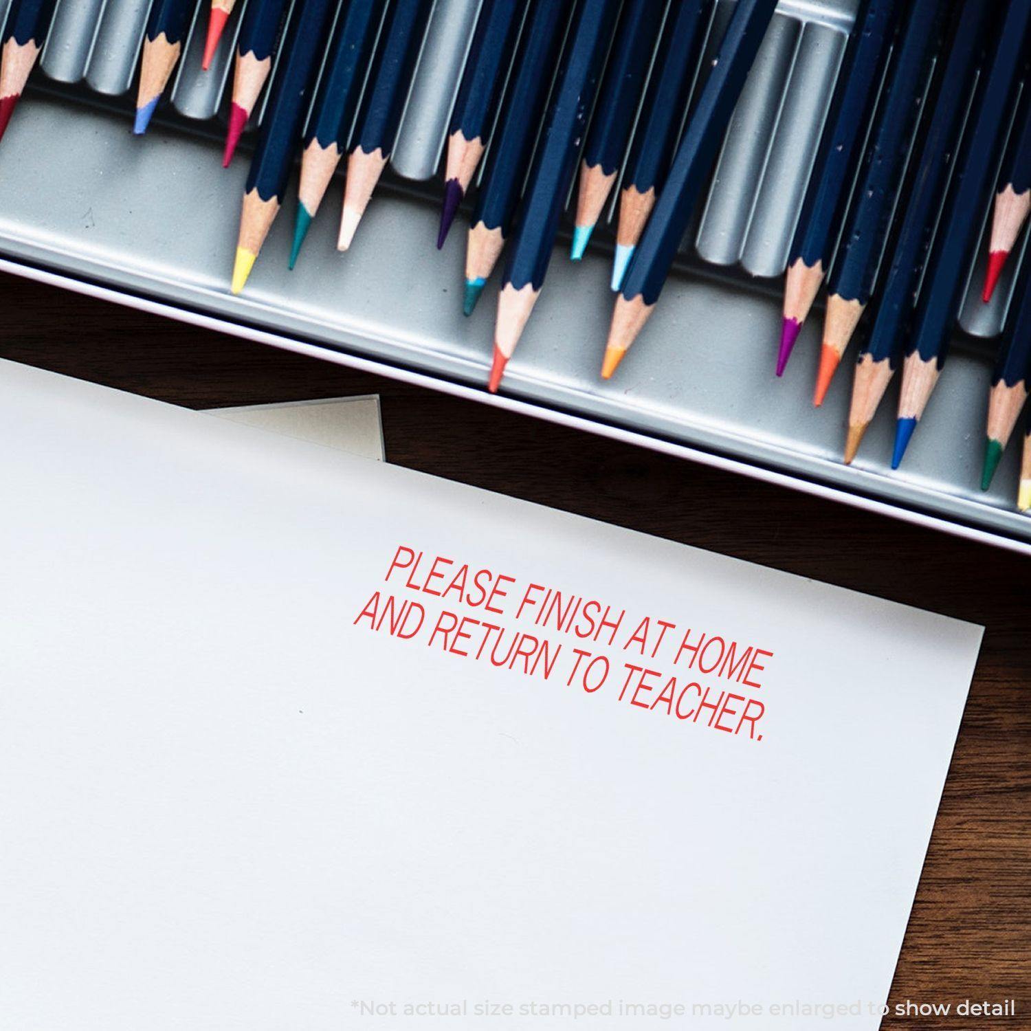 Slim Pre-Inked Please Finish At Home And Return To Teacher Stamp in red ink on paper, with colored pencils in the background.