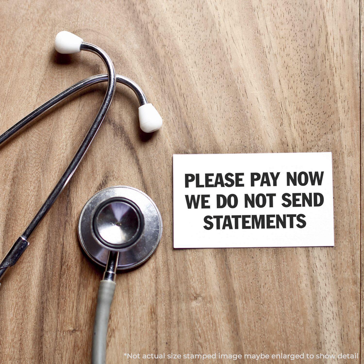 A stethoscope on a wooden surface next to a Large Self Inking Please Pay Now No Statements Stamp impression on a white card.