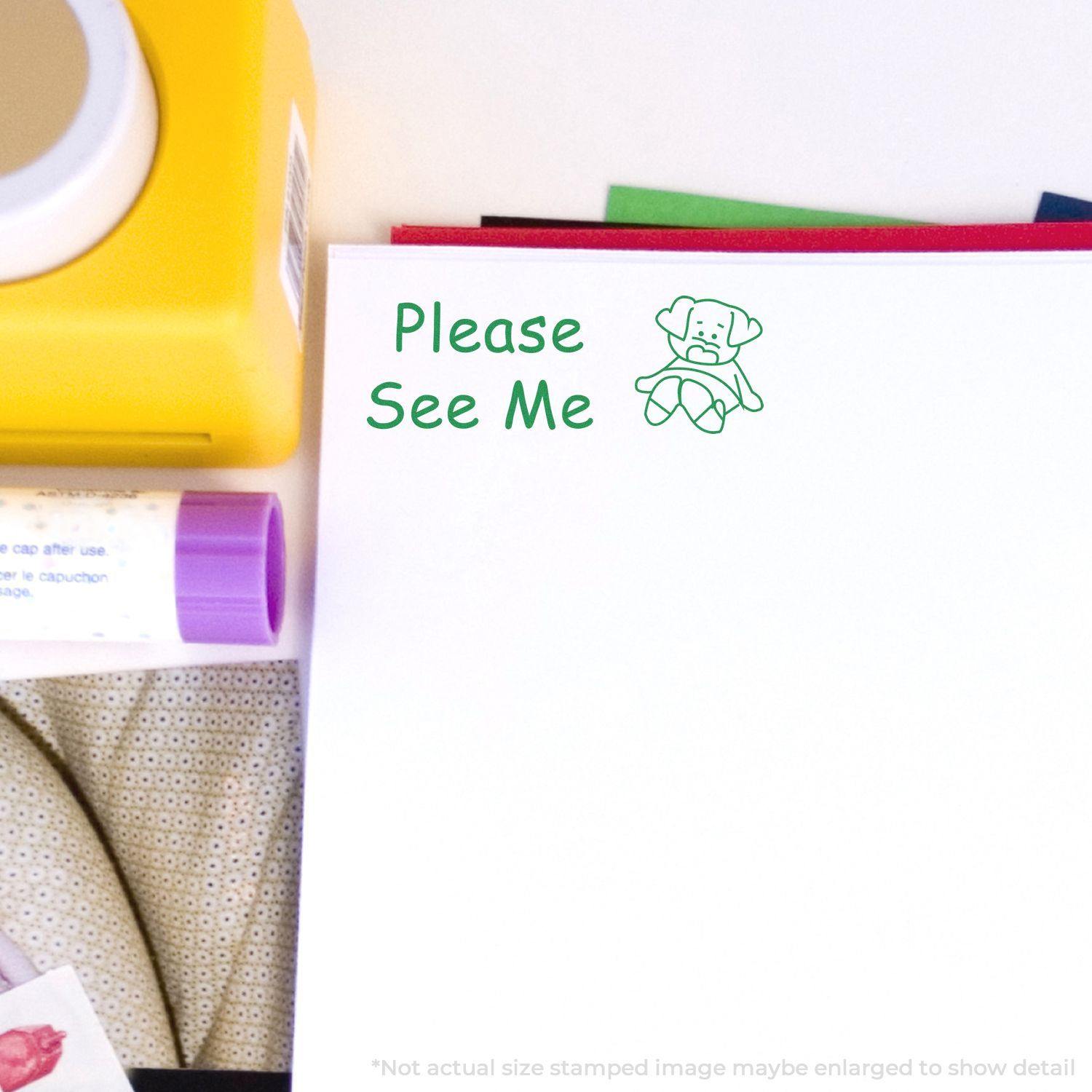 Please See Me rubber stamp imprint in green ink on white paper, surrounded by office supplies including a yellow tape dispenser.