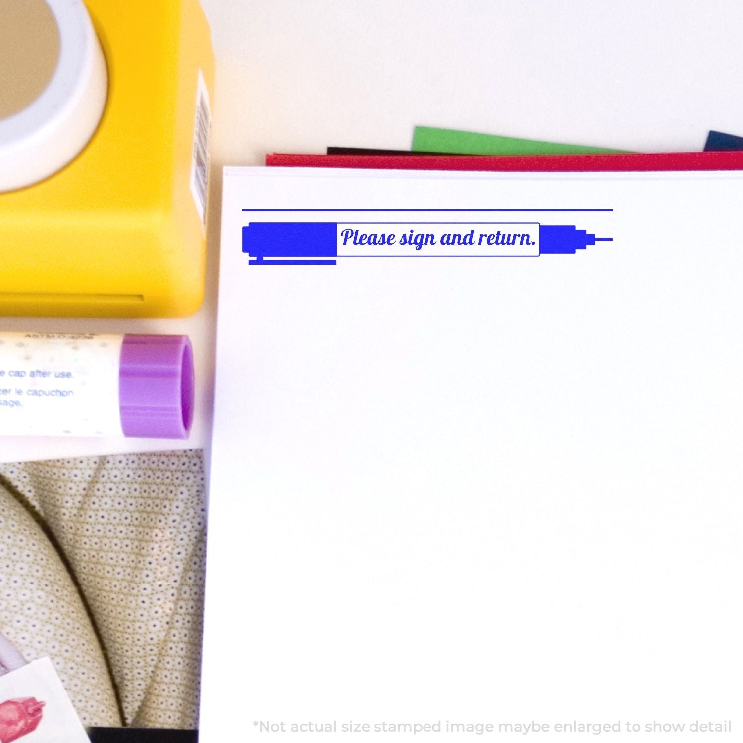 Self Inking Please Sign and Return with Pen Stamp used on a document, surrounded by office supplies including a yellow box and glue stick.