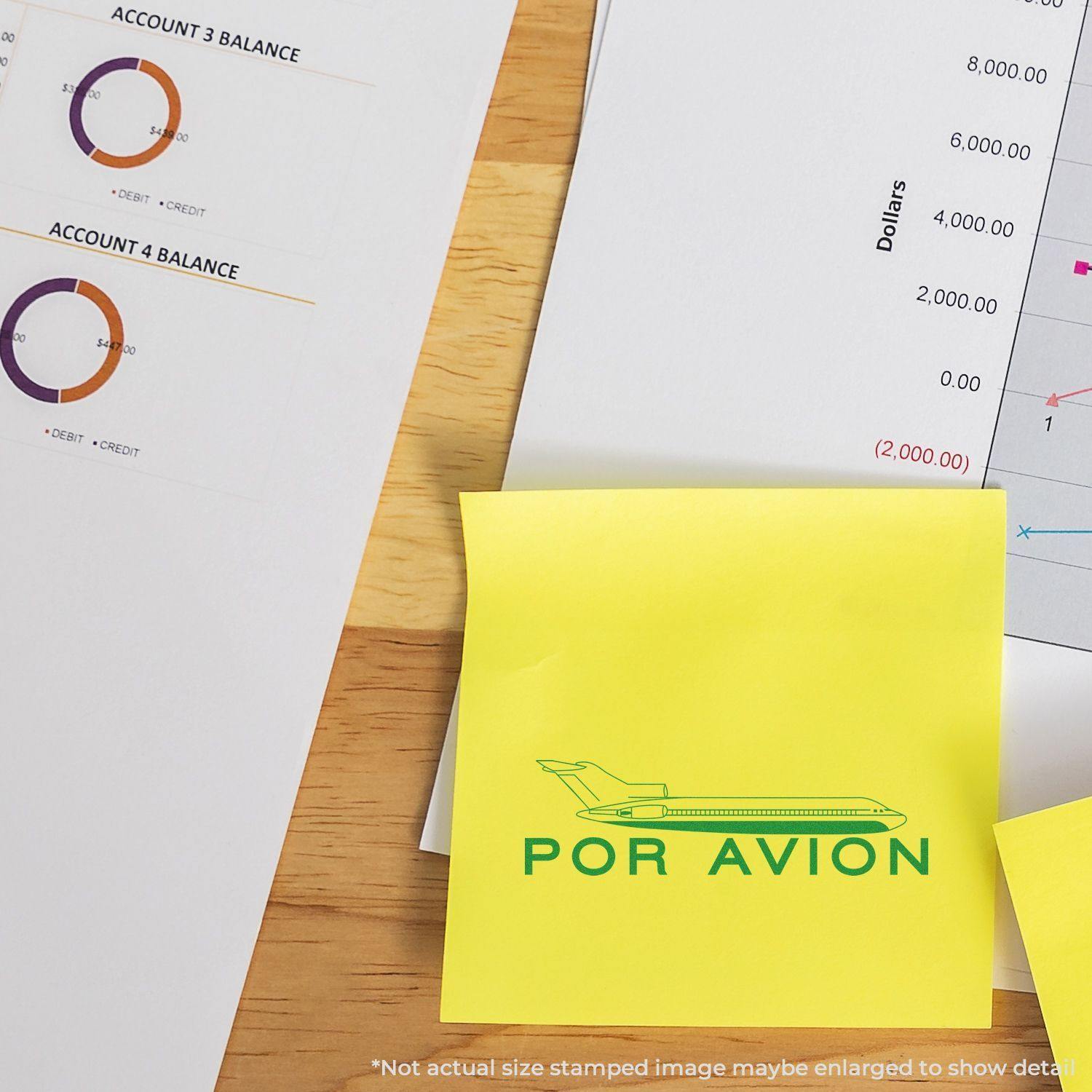 Large Por Avion Rubber Stamp used on a yellow sticky note, placed on a desk with financial documents and charts.