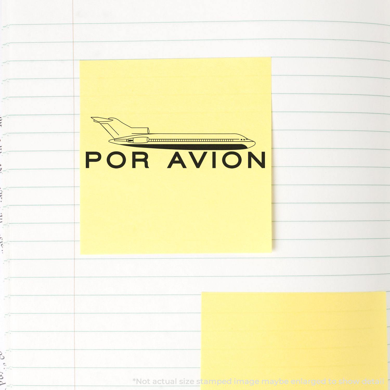 Large Self Inking Por Avion Stamp on a yellow sticky note with a plane icon, placed on a lined notebook page.