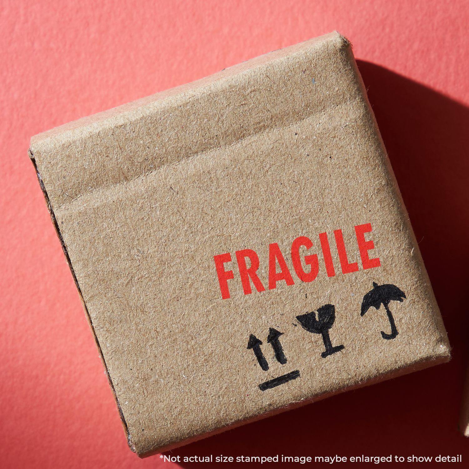 Cardboard box with a red Fragile rubber stamp and handling symbols on a red background.