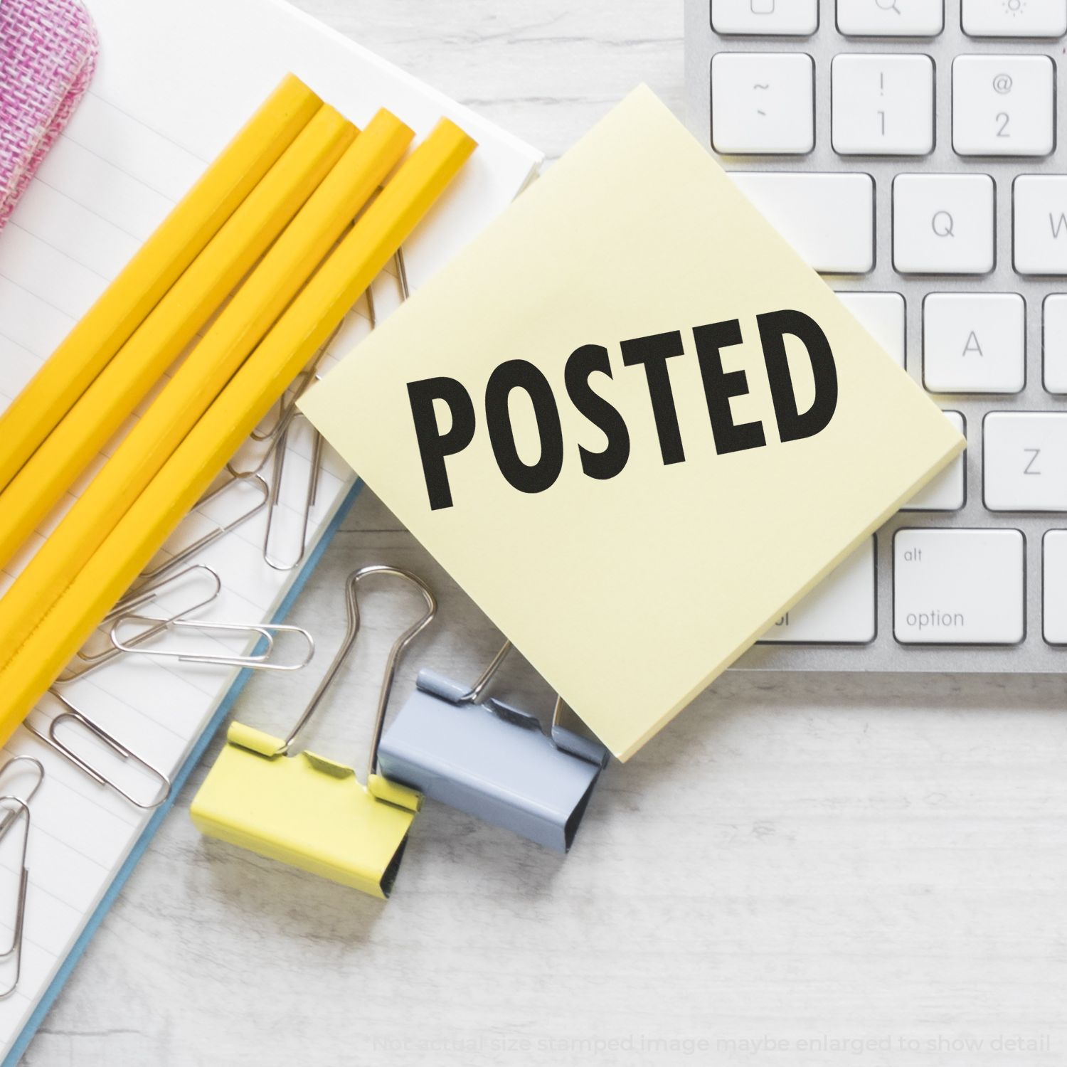 Self Inking Posted Stamp on a yellow sticky note beside pencils, paper clips, and a keyboard on a desk.