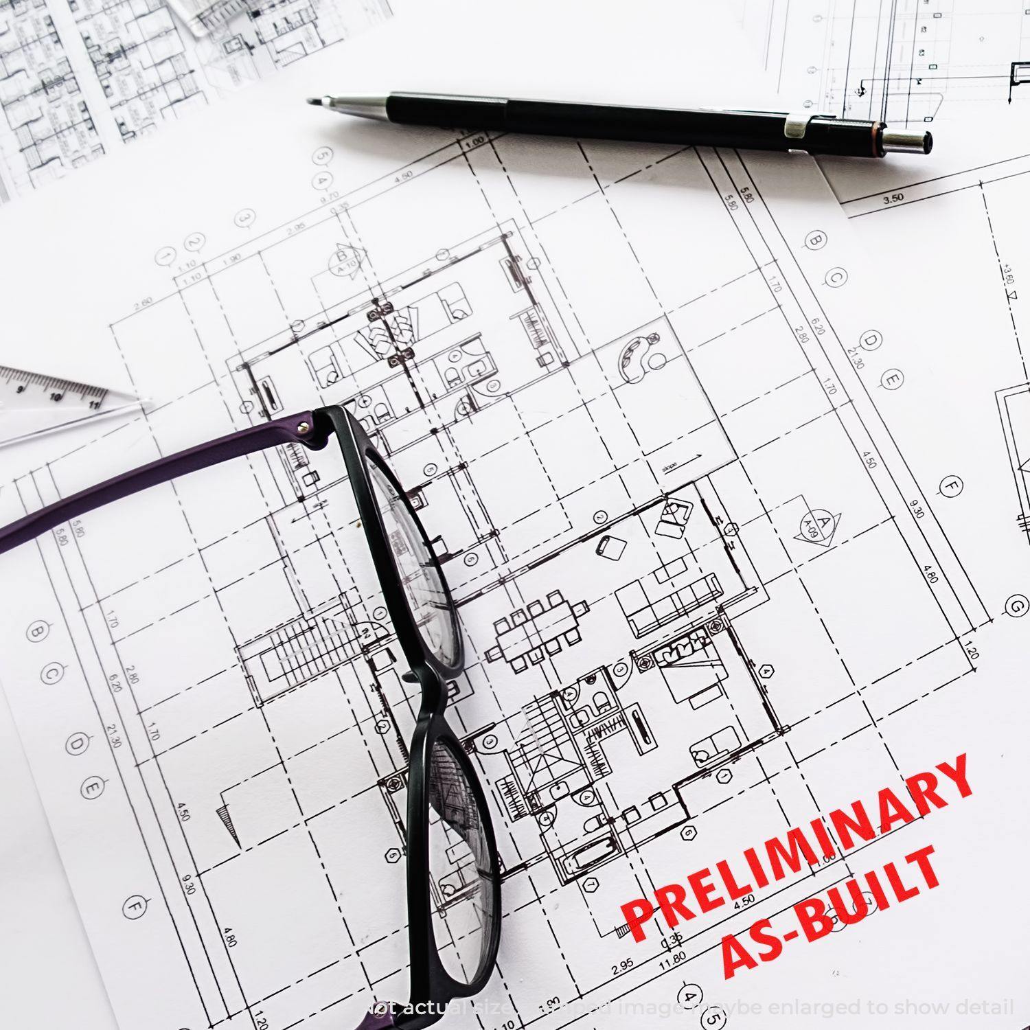 Architectural plans stamped with Large Self Inking Preliminary As-Built Stamp, with glasses and a pen placed on top.