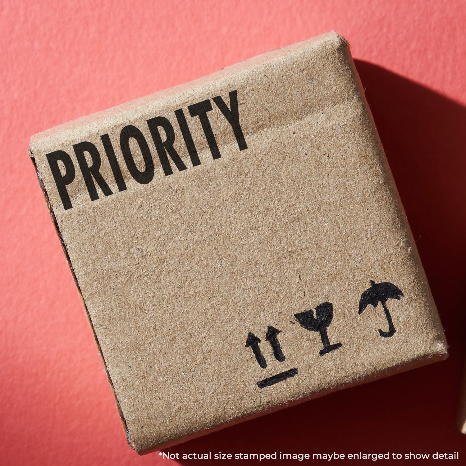 A cardboard box stamped with PRIORITY using a Self Inking Priority Mailing Stamp, placed on a red surface.