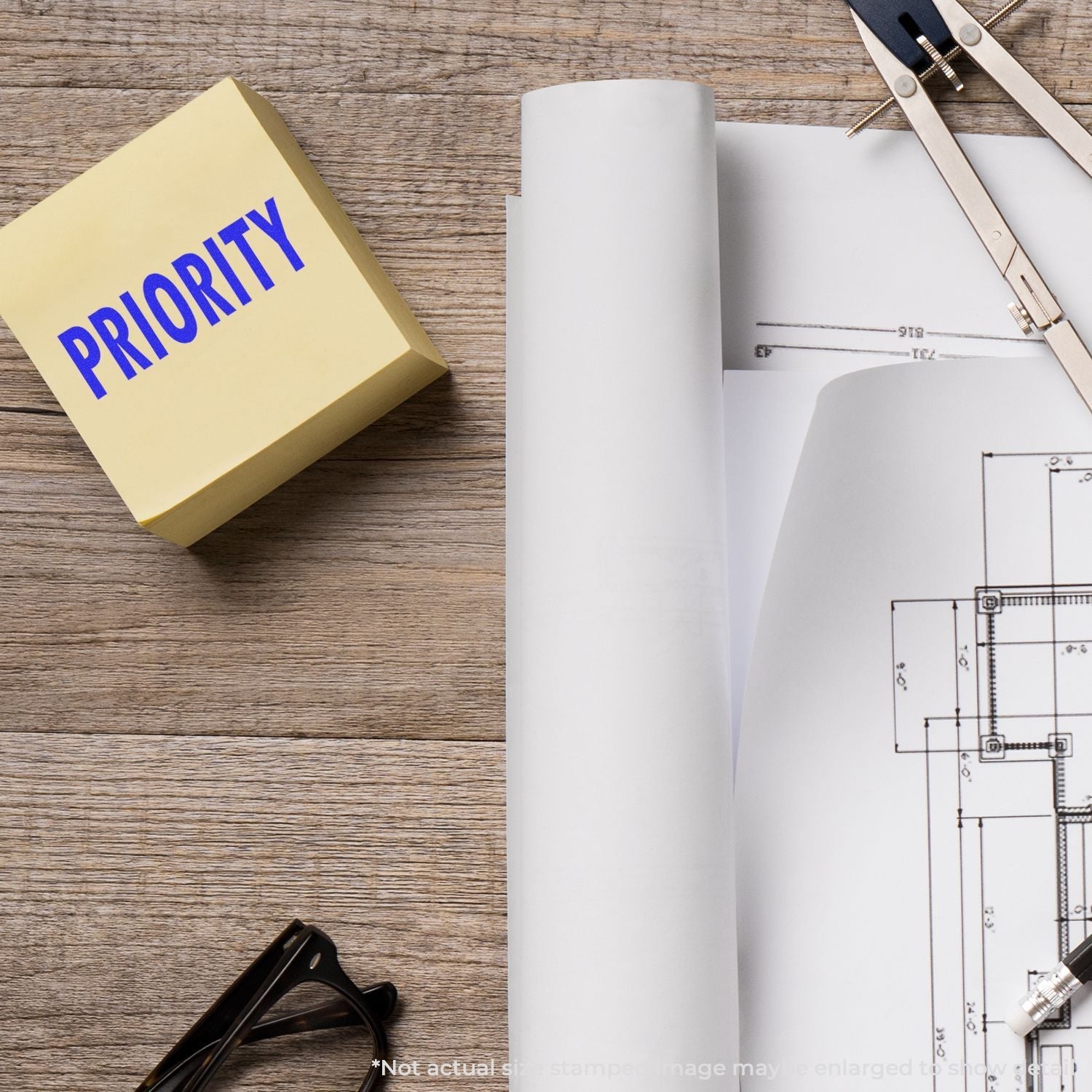 Self Inking Priority Mailing Stamp on a wooden desk with architectural plans, a compass, and glasses.