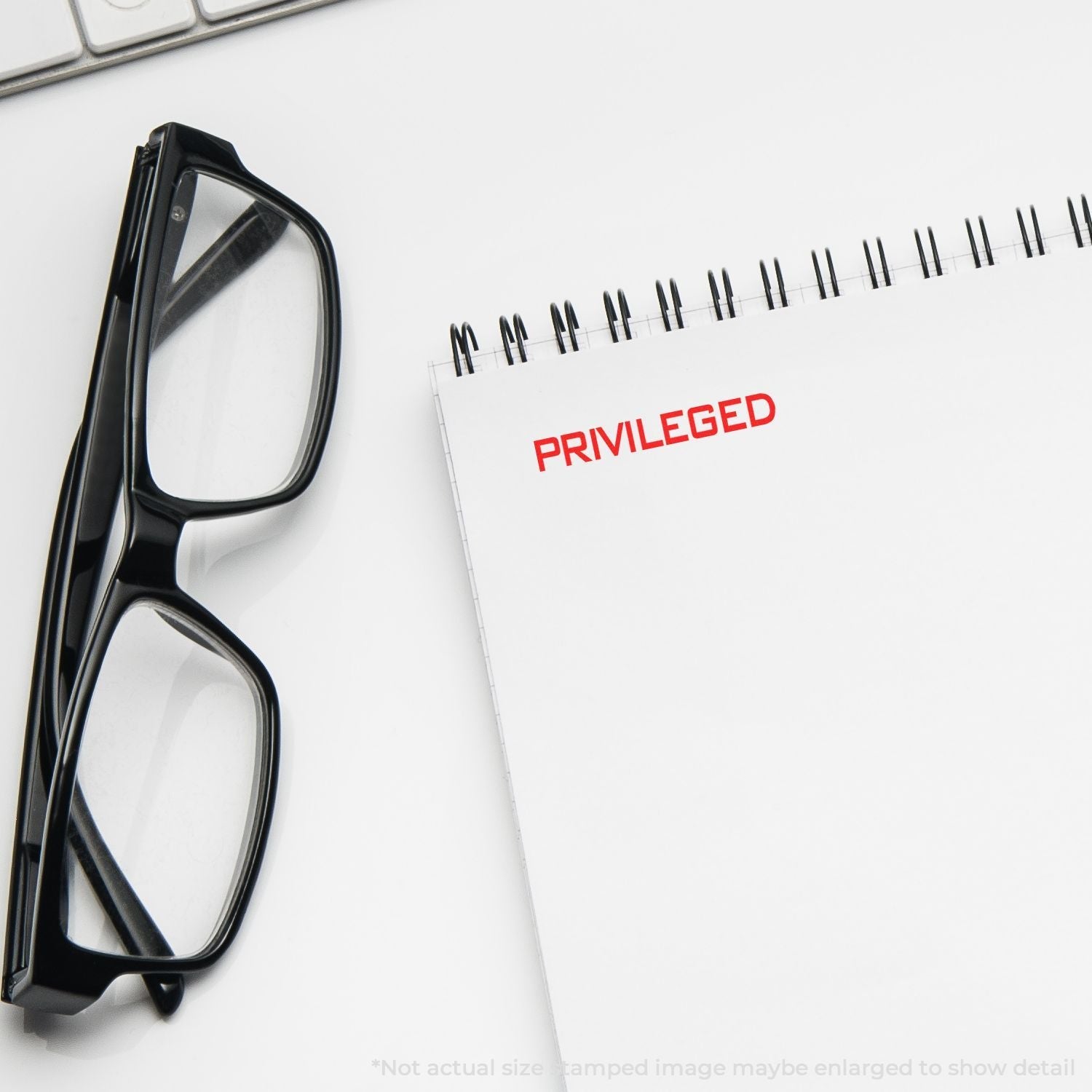 Self Inking Privileged Stamp marking PRIVILEGED in red on a spiral notebook, with black glasses and a keyboard nearby.