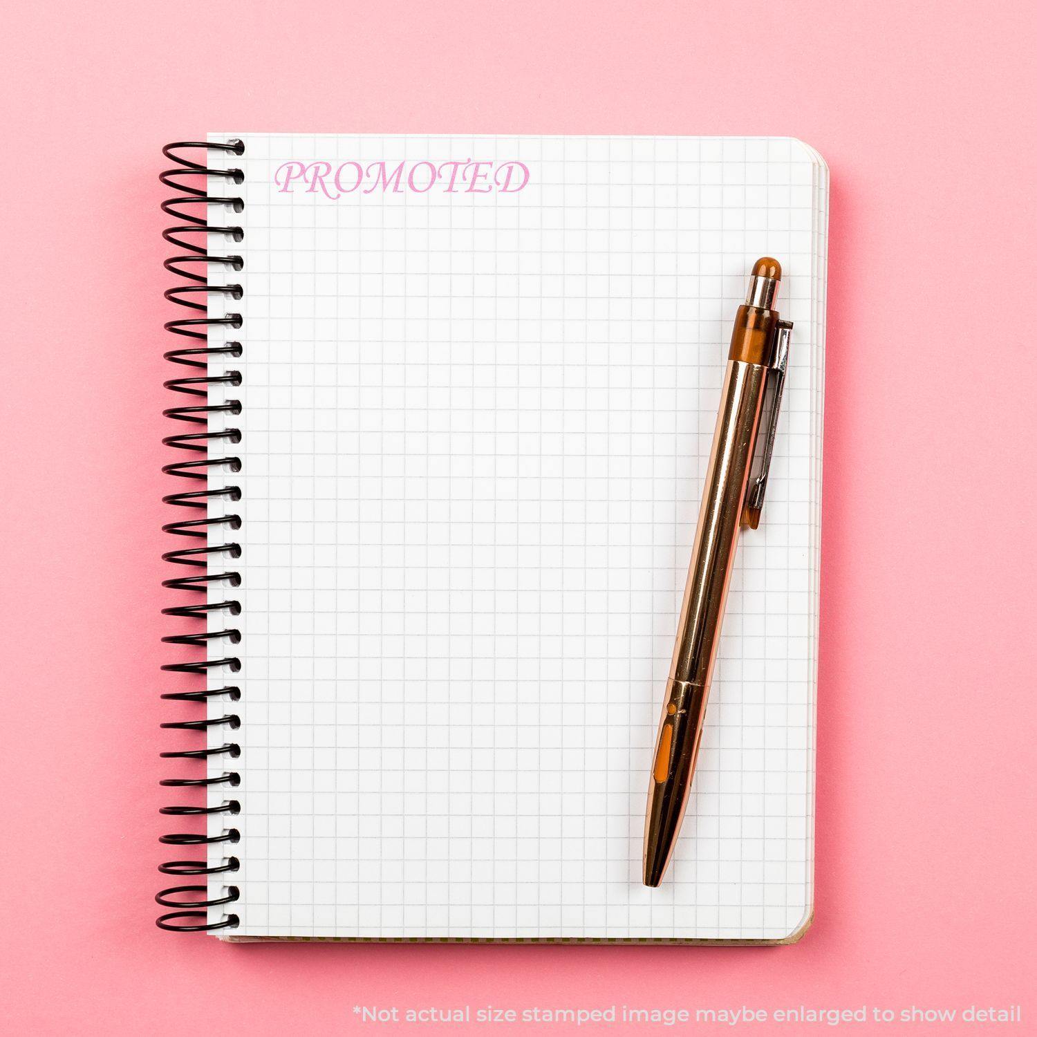 Large Pre-Inked Promoted Stamp used on a spiral notebook with a pen on a pink background.