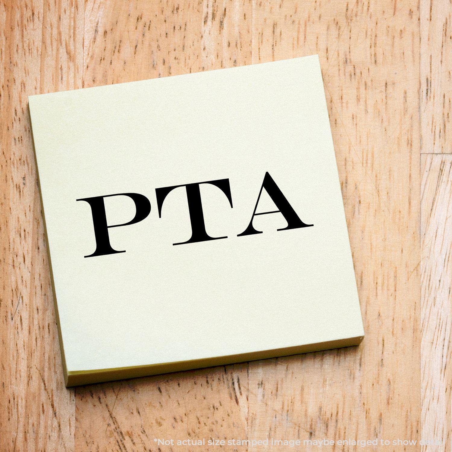 Large Pre-Inked PTA Stamp imprint on a yellow sticky note placed on a wooden surface.