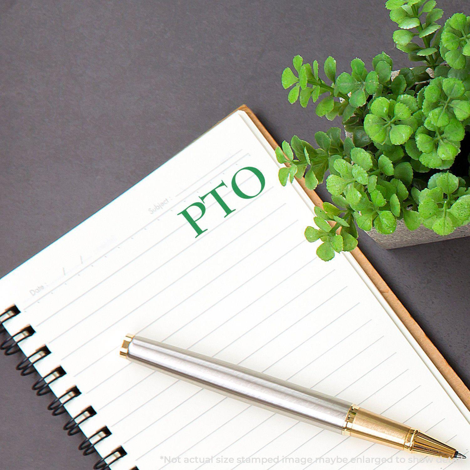 Large Pre-Inked PTO Stamp used on a notebook page next to a pen and a small potted plant.