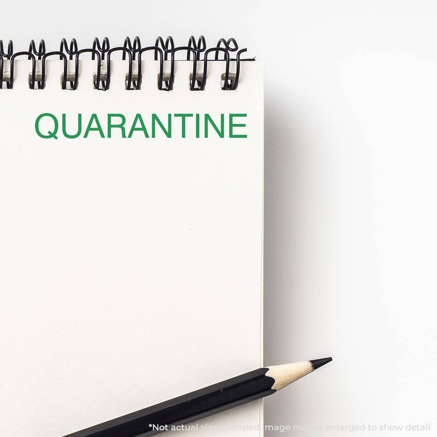 A Large Quarantine Rubber Stamp imprint on a white notepad with a black pencil beside it. The word QUARANTINE is stamped in green ink.