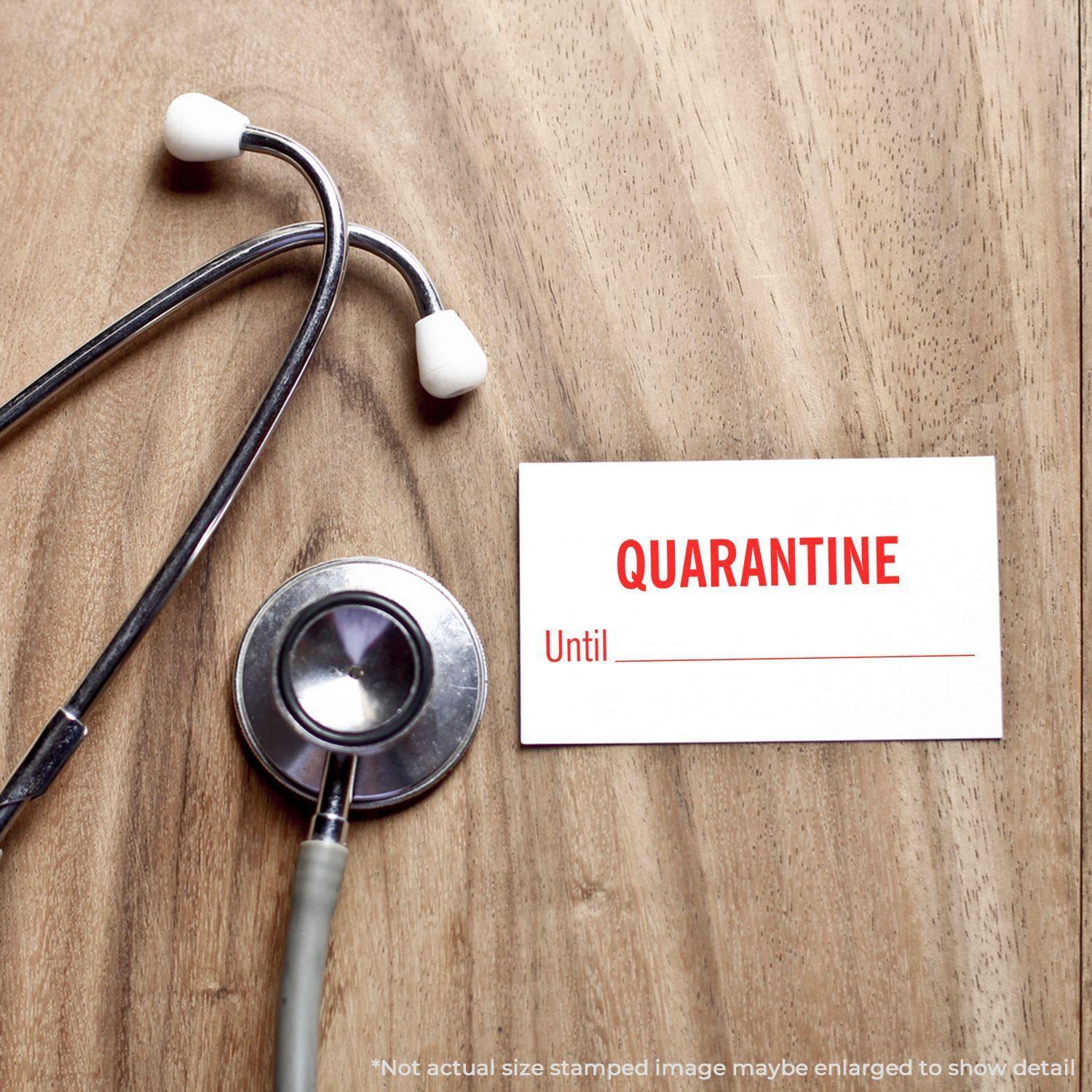 A Large Pre-Inked Quarantine Until Stamp on a wooden surface next to a stethoscope, with a stamped card reading QUARANTINE Until _______ .