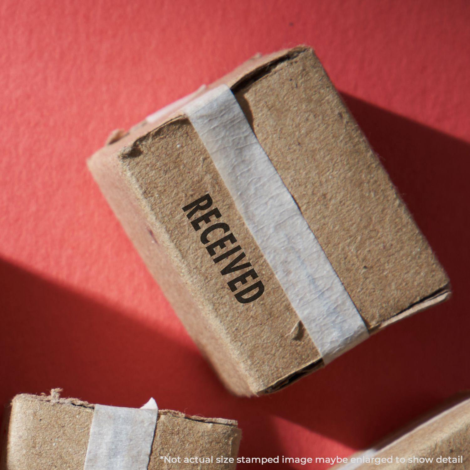 A cardboard box stamped with RECEIVED using the Large Received Rubber Stamp, placed on a red surface.