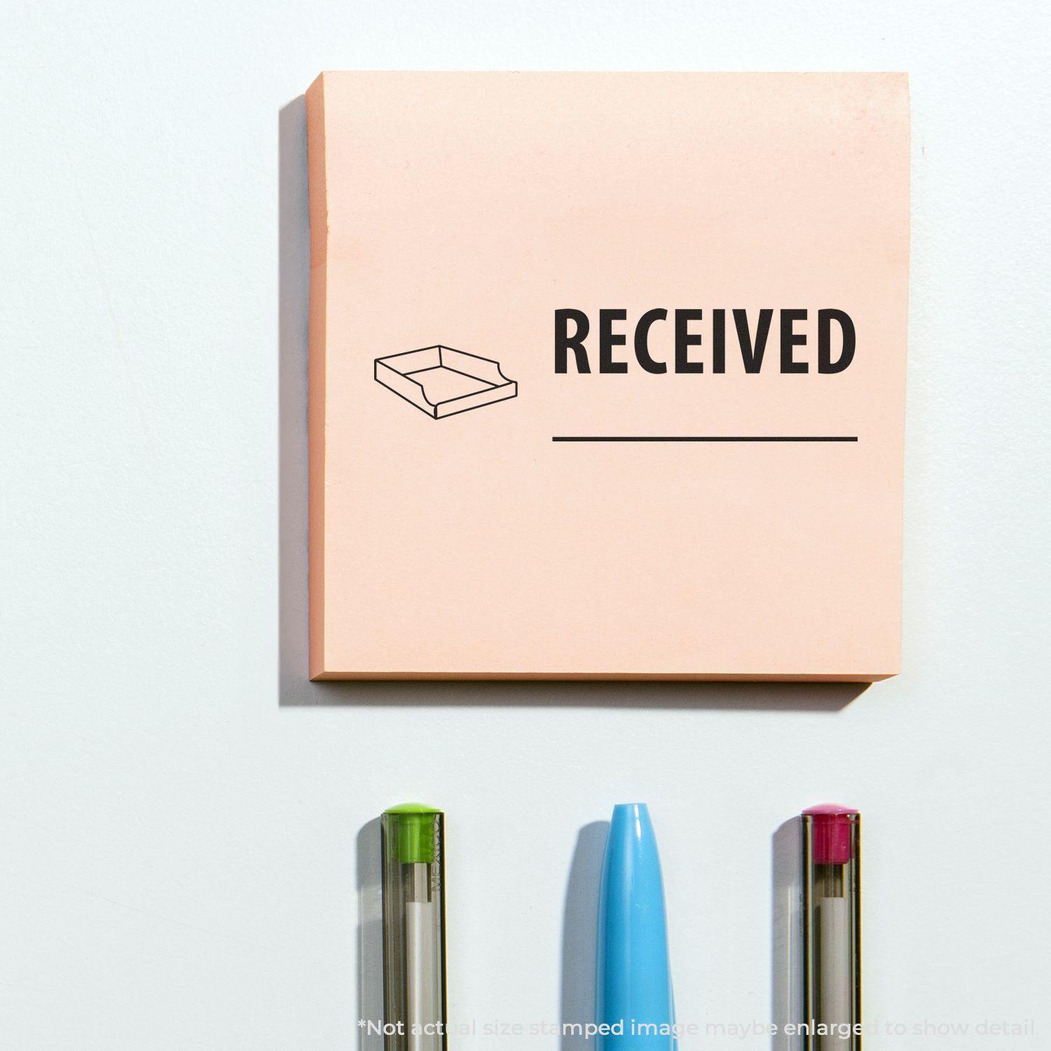 Received with Box Rubber Stamp on a pink sticky note, with three pens below it on a white surface.