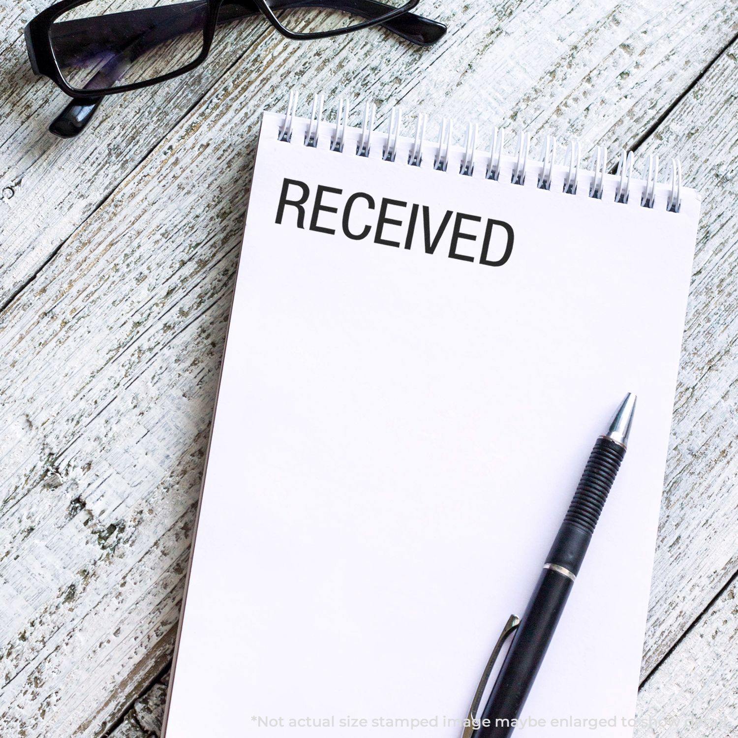 Large Pre-Inked Received Stamp used on a white notepad with a pen and glasses on a wooden surface.