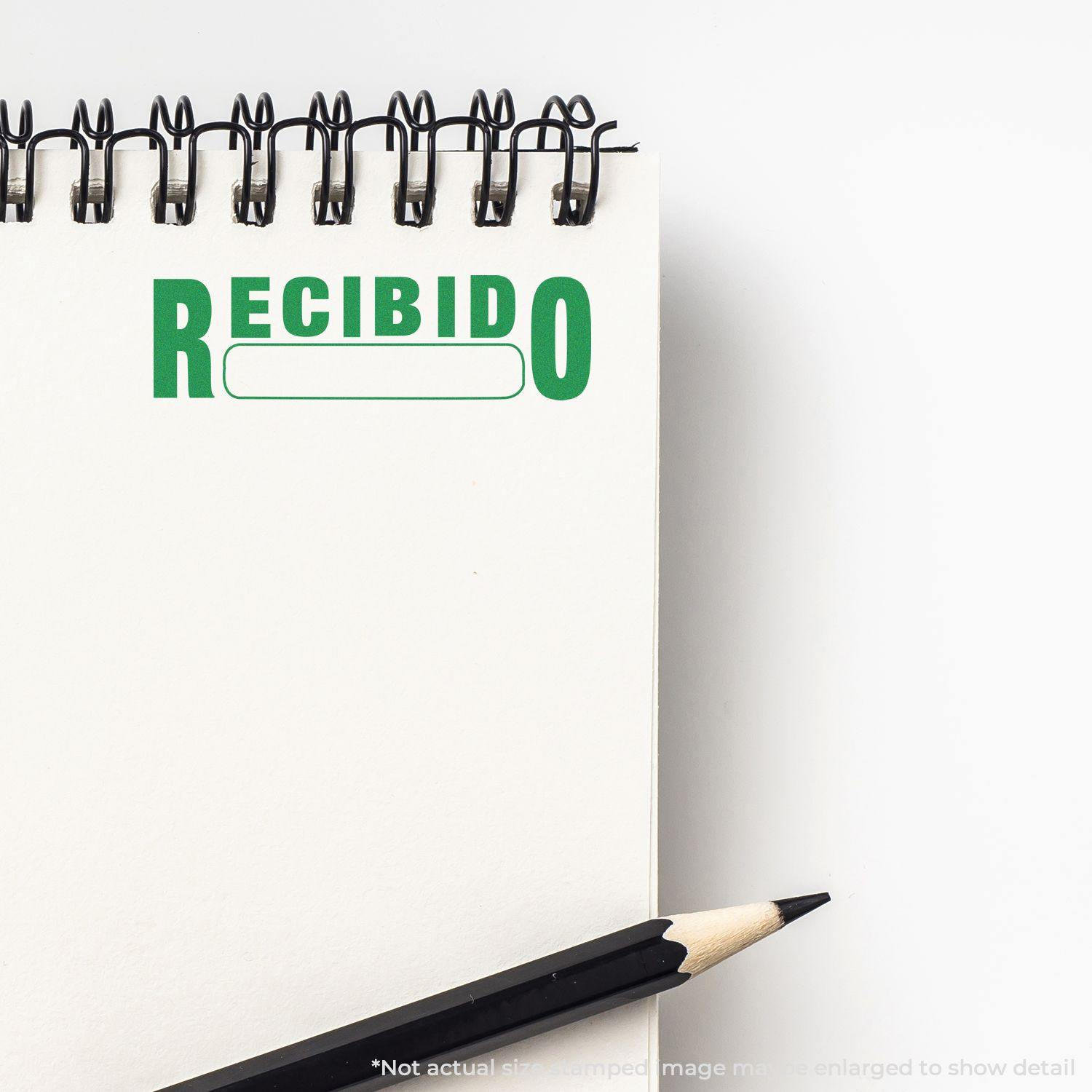 A Large Pre-Inked Recibido Stamp imprint in green ink on a spiral notebook page, with a pencil placed beside the notebook.