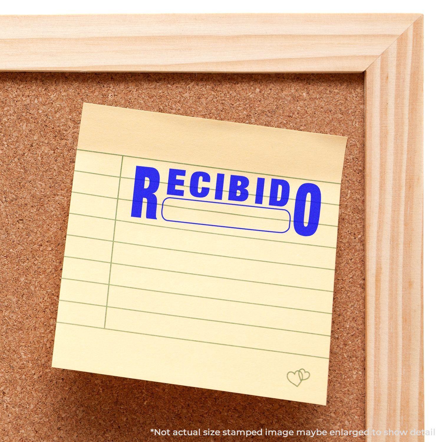 A corkboard with a yellow note stamped RECIBIDO in blue ink using the Large Pre-Inked Recibido Stamp.