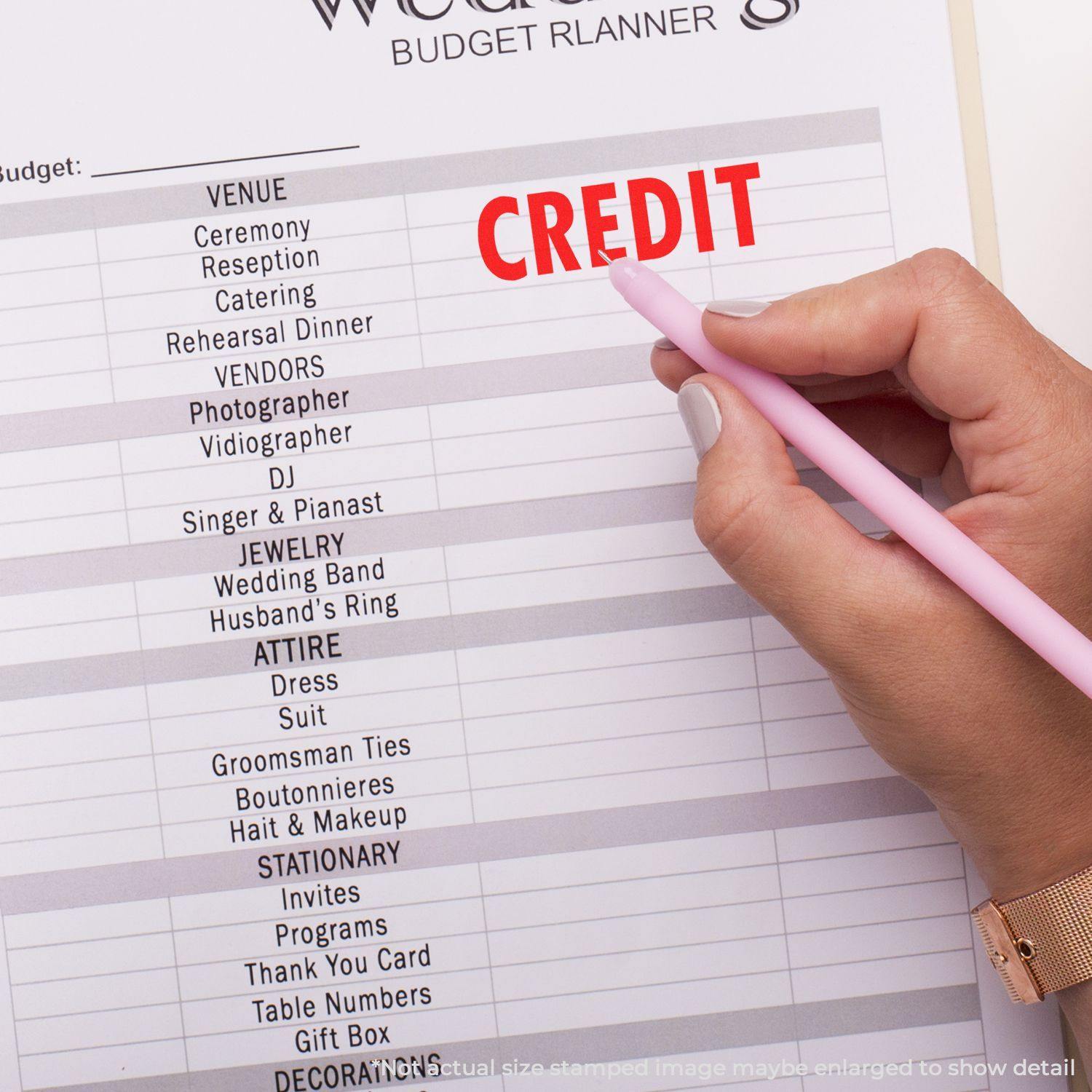 Hand holding a pink pen marking CREDIT with a red credit rubber stamp on a budget planner sheet.