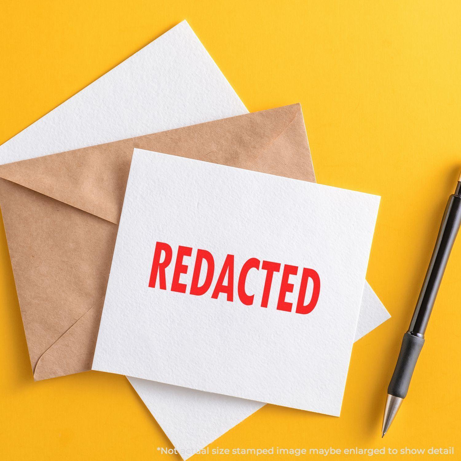 Slim Pre-Inked Redacted Stamp used on a white card with a brown envelope and a black pen on a yellow background.