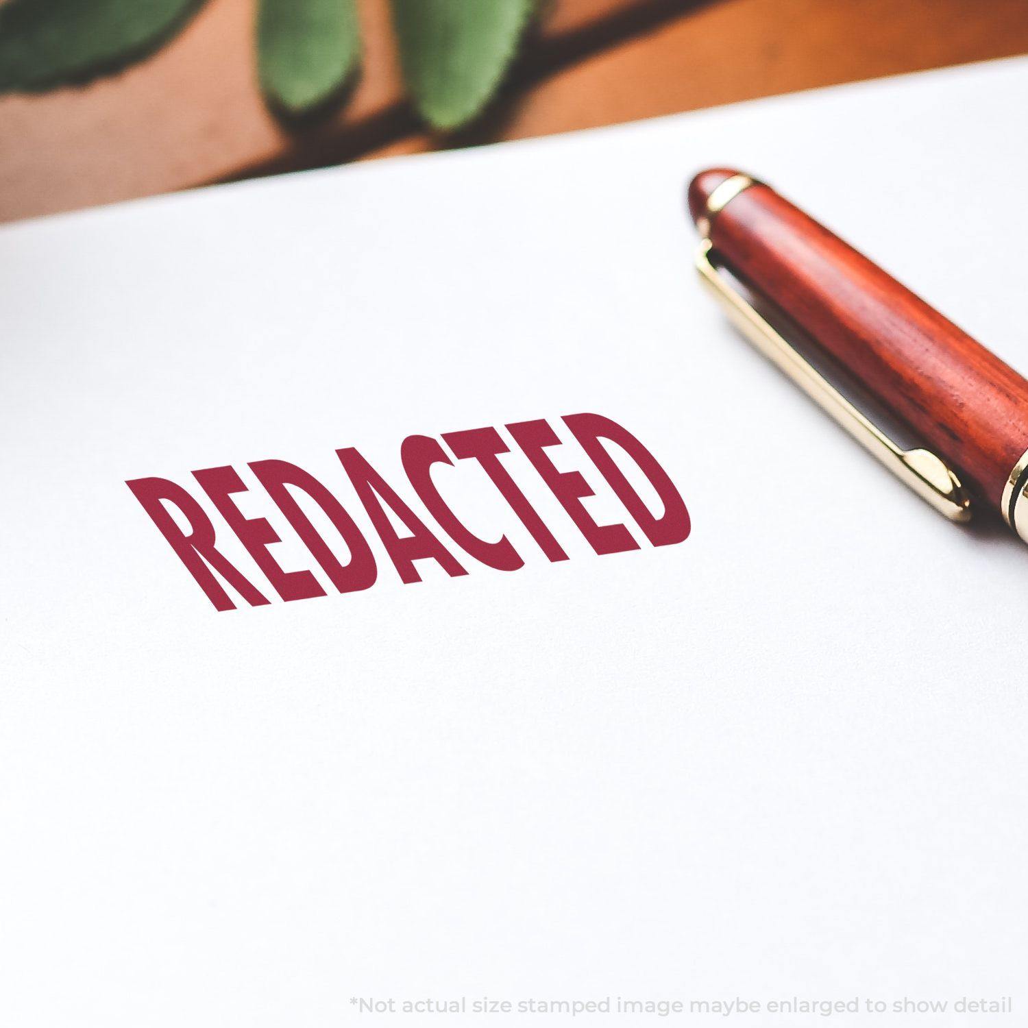 Large Pre-Inked Redacted Stamp in use, showing the word REDACTED stamped in red ink on white paper with a pen nearby.