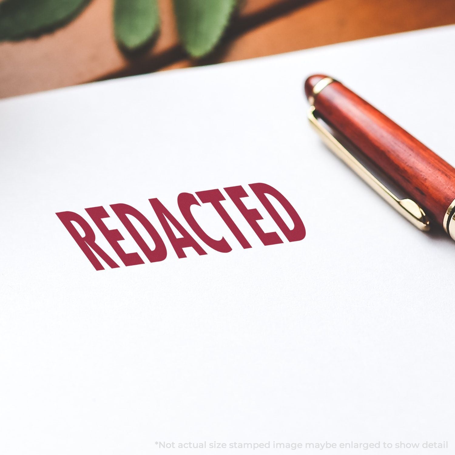 Self Inking Redacted Stamp imprint on white paper, with a red pen nearby. The word REDACTED is clearly visible in bold red letters.