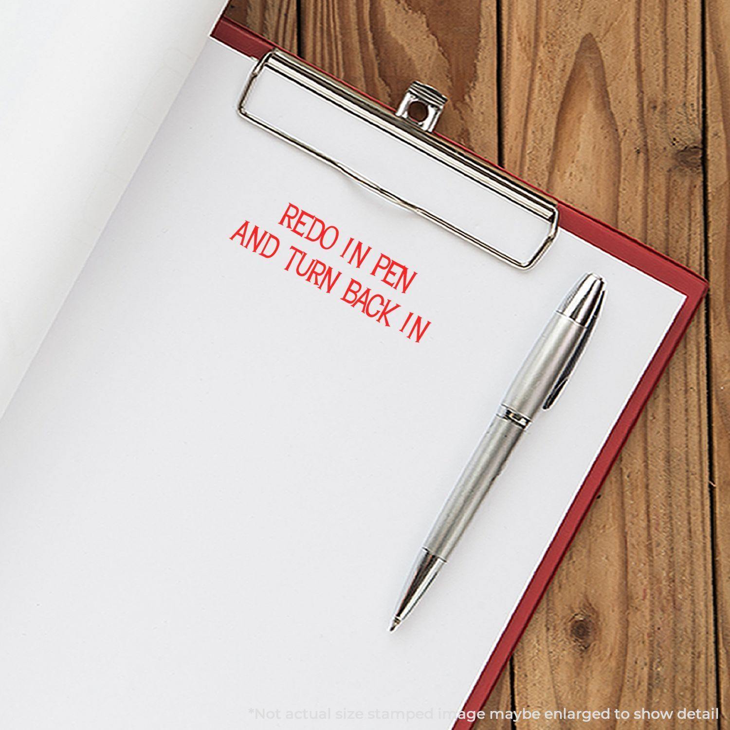 Clipboard with paper stamped REDO IN PEN AND TURN BACK IN in red ink, next to a pen on a wooden surface.