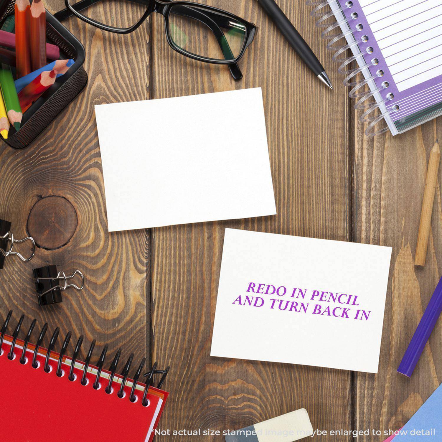 Desk with stationery, two cards, one stamped with Large Redo In Pencil And Turn Back In Rubber Stamp in purple, glasses, and notebooks.