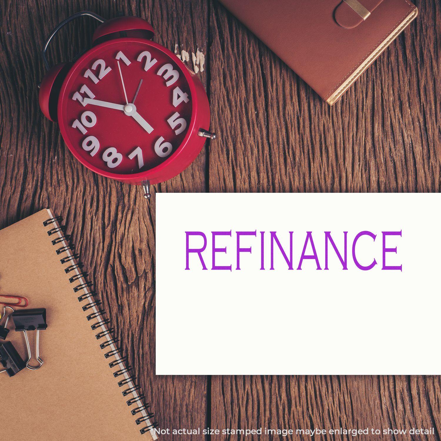 Refinance rubber stamp on a white card, surrounded by a red clock, notebook, binder clips, and a leather wallet on a wooden table.