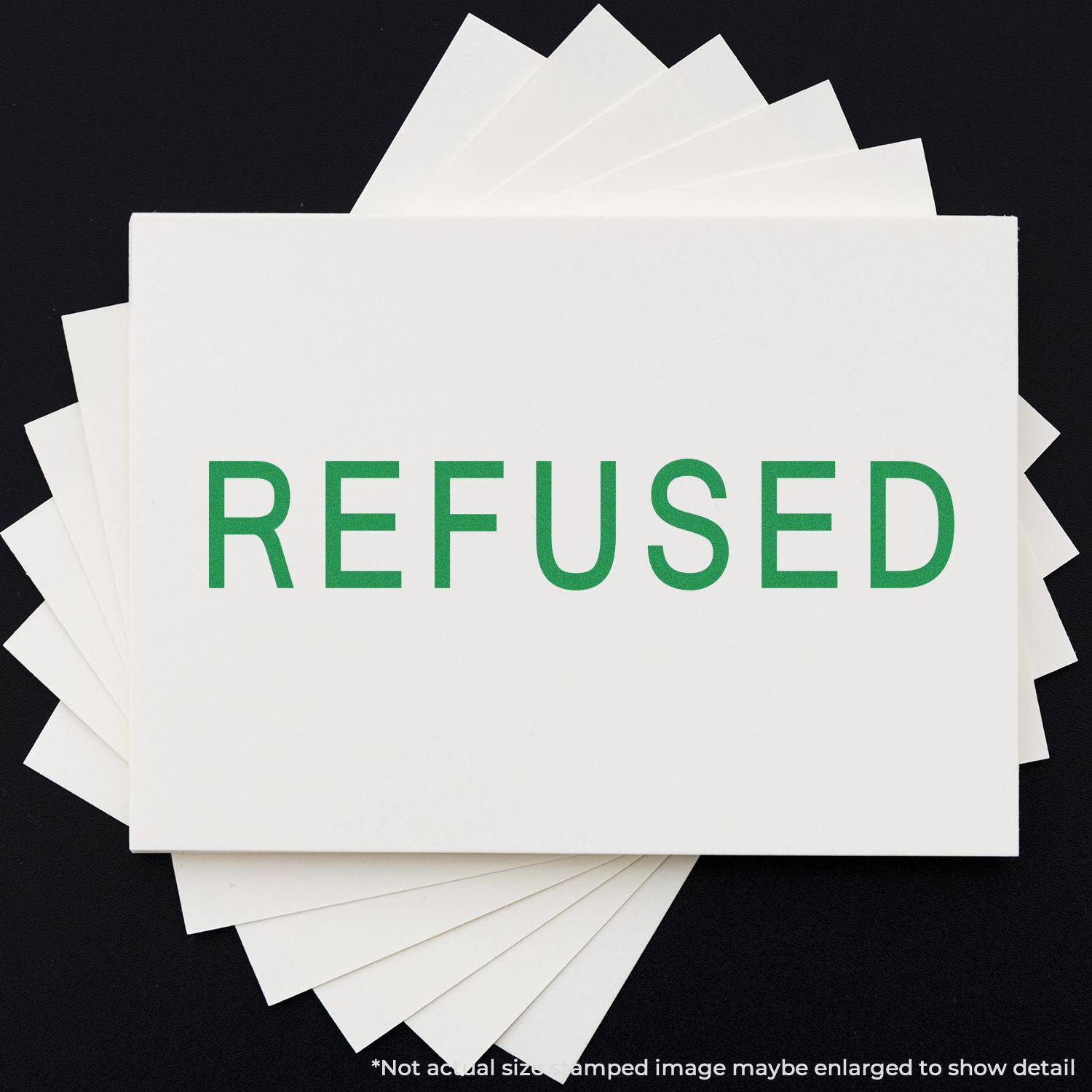 Large Refused Rubber Stamp in green ink on white paper, displayed on a black background with multiple sheets fanned out underneath.