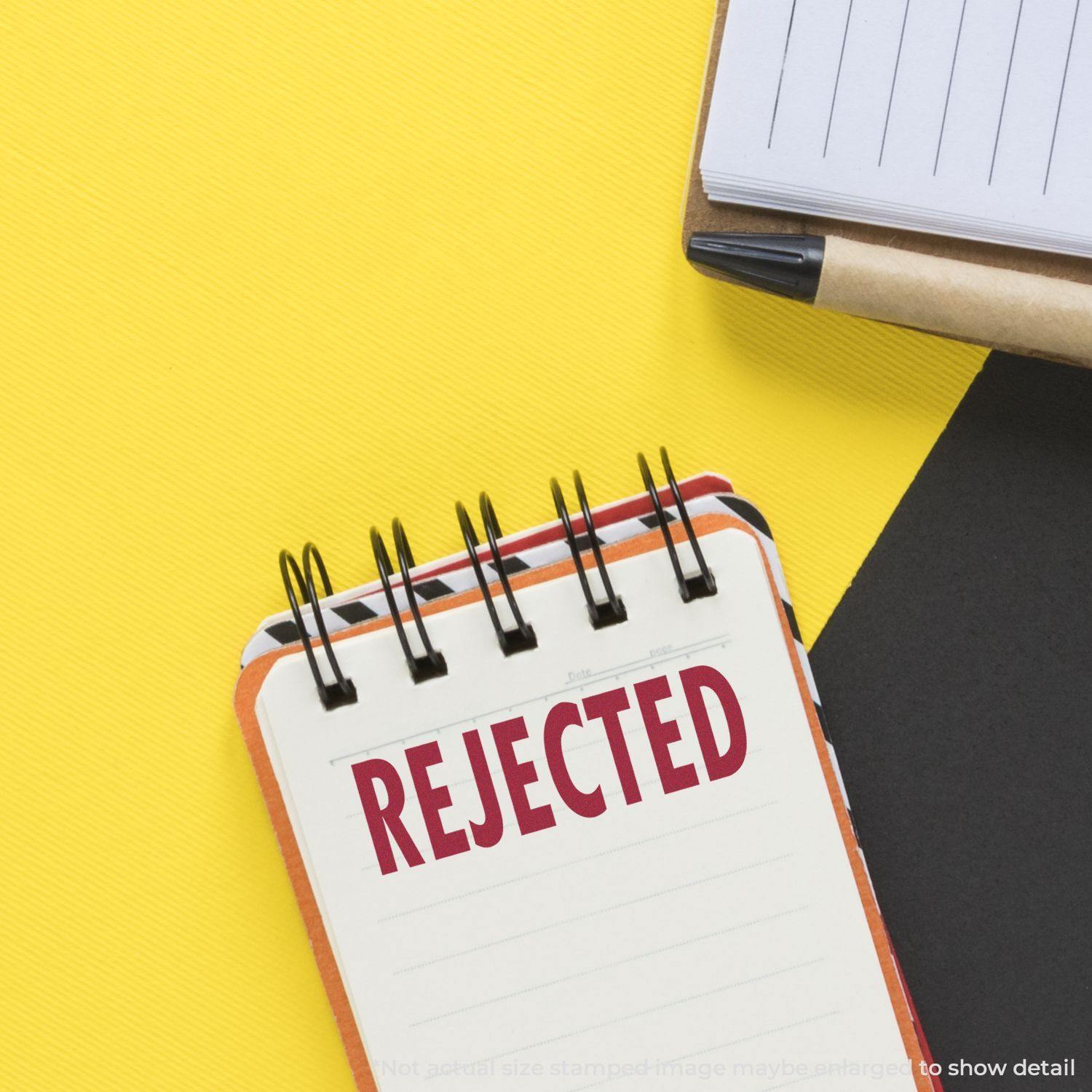 A notebook with REJECTED stamped in red using the Large Pre-Inked Rejected Stamp, placed on a yellow and black background.