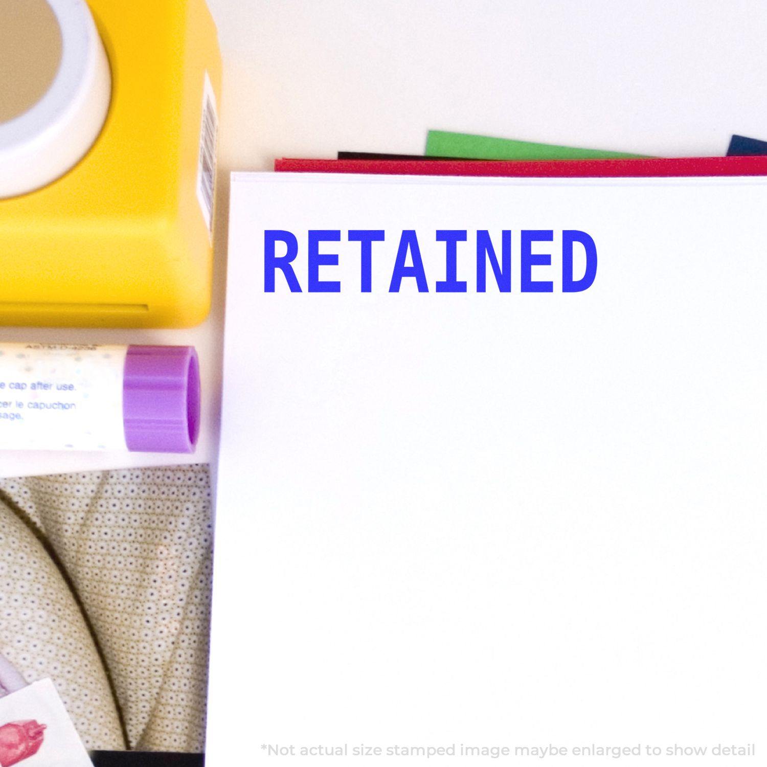 Large Self Inking Retained Stamp in blue ink on white paper, surrounded by office supplies including a yellow container and a purple glue stick.