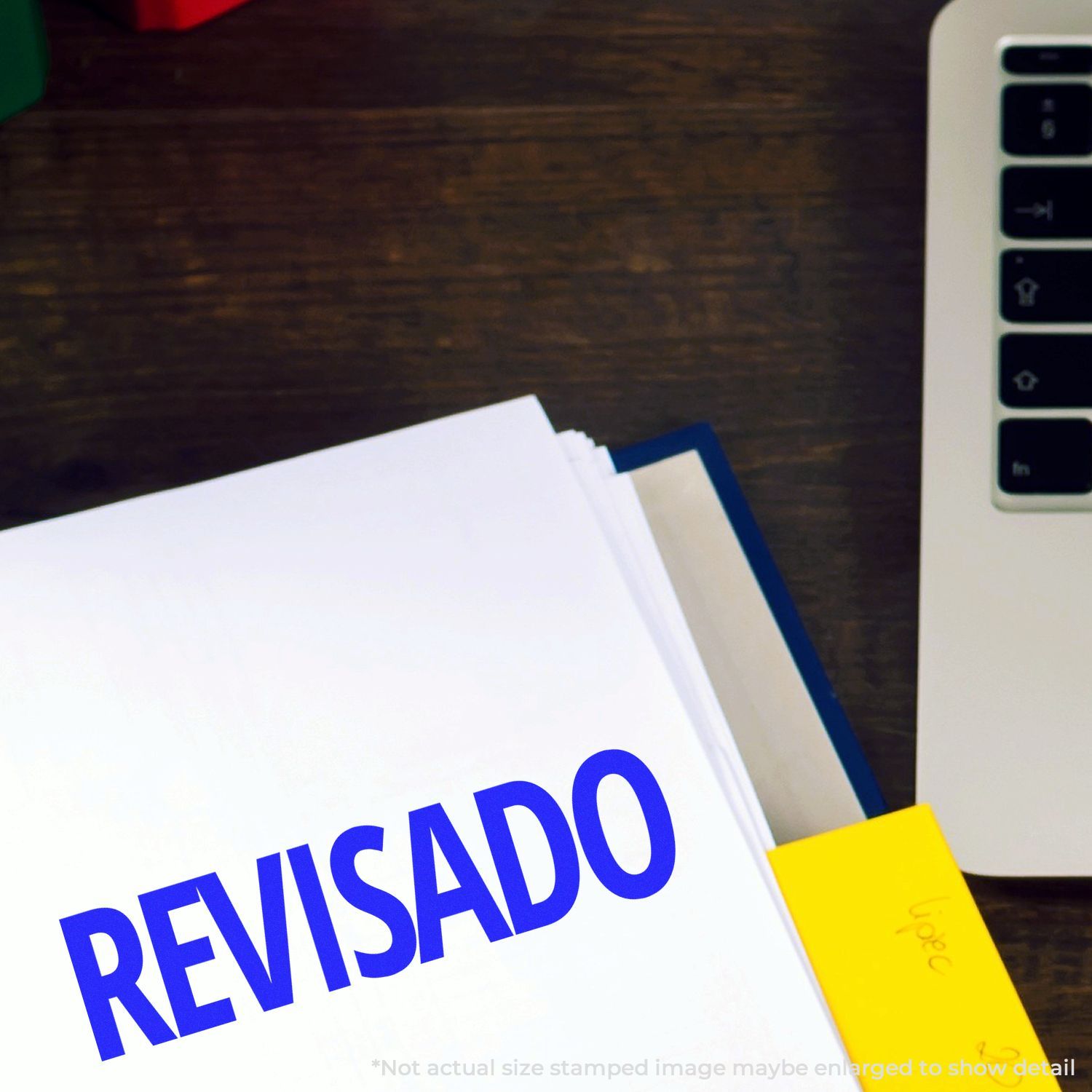 A document stamped with REVISADO using the Self Inking Revisado Stamp, placed next to a laptop and a yellow sticky note.