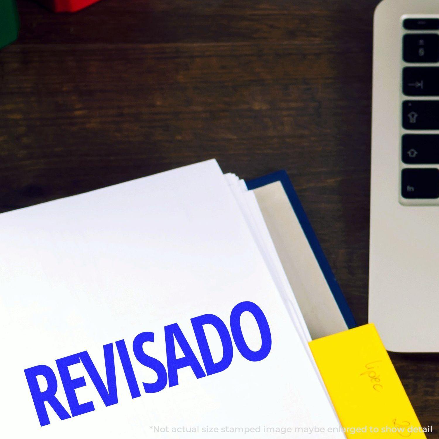 Large Revisado Rubber Stamp marking a document with REVISADO in blue ink, next to a laptop on a wooden desk.