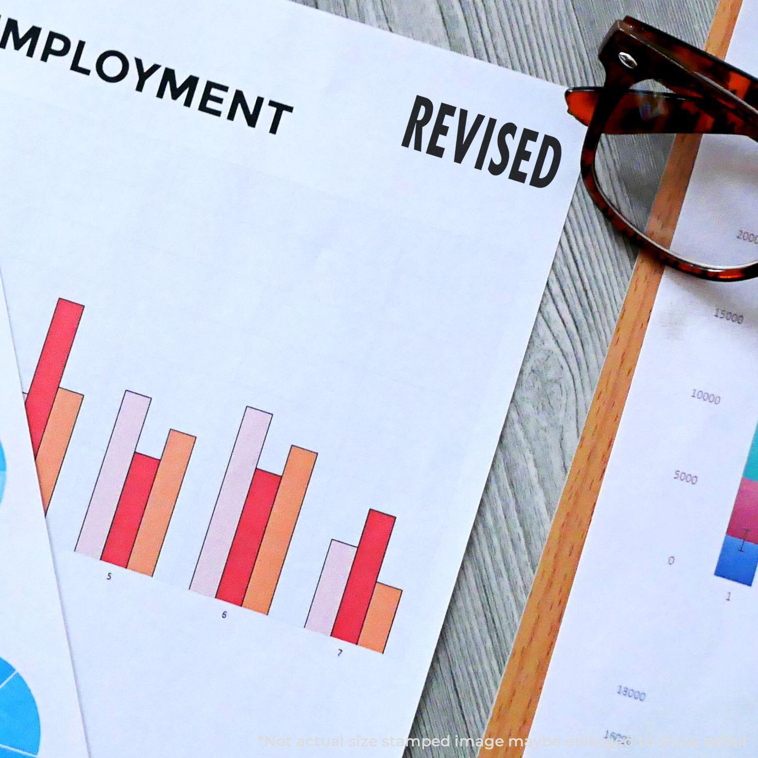 Employment document with a bar chart stamped REVISED using a Slim Pre-Inked Bold Revised Stamp, next to glasses on a desk.