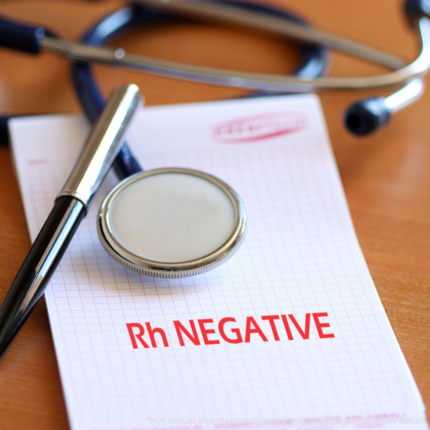 A stethoscope, pen, and Large Pre-Inked Rh Negative Stamp on a notepad with Rh NEGATIVE stamped in red.