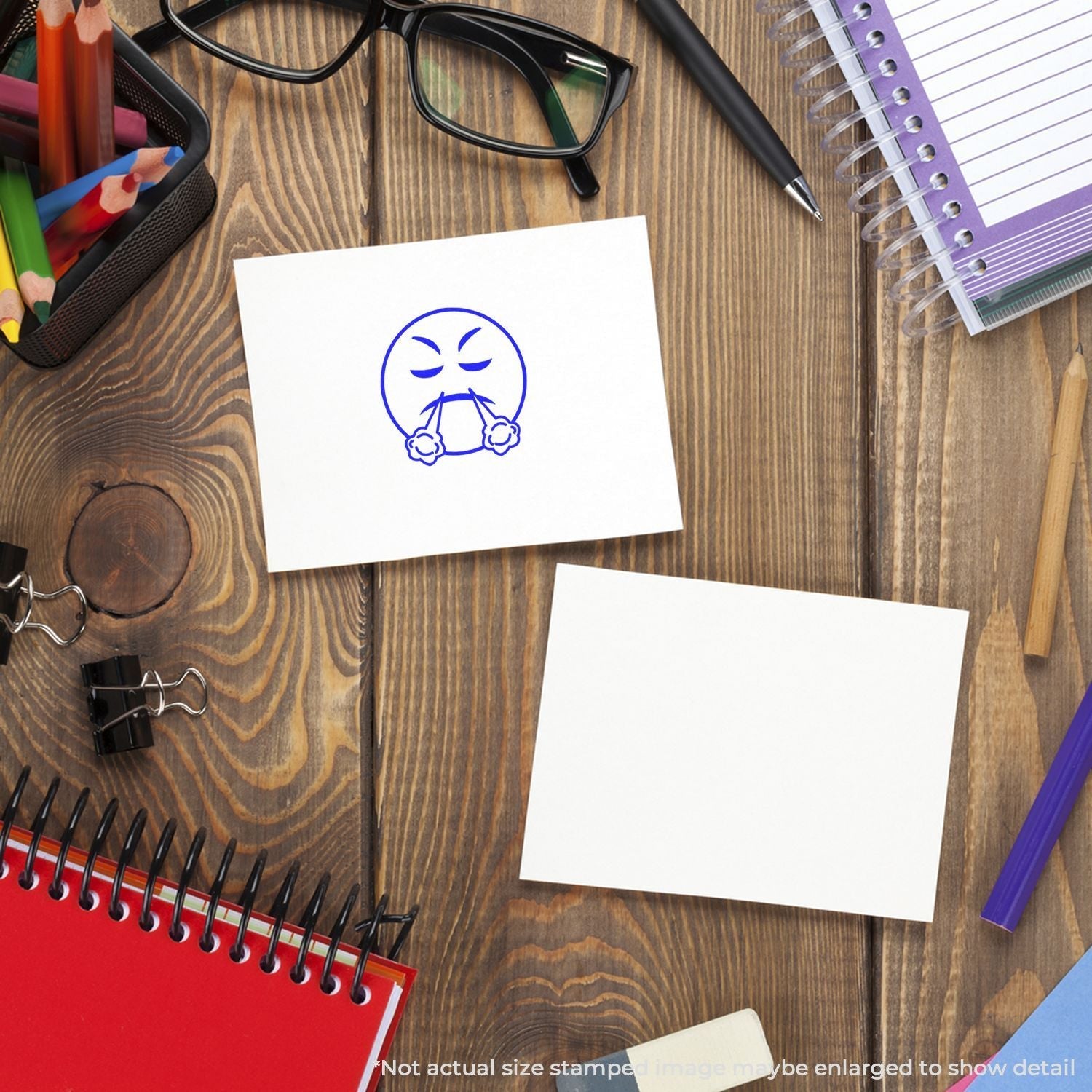 A desk with stationery and a card stamped with the Self Inking Round Angry Smiley Stamp, showing an angry face in blue ink.