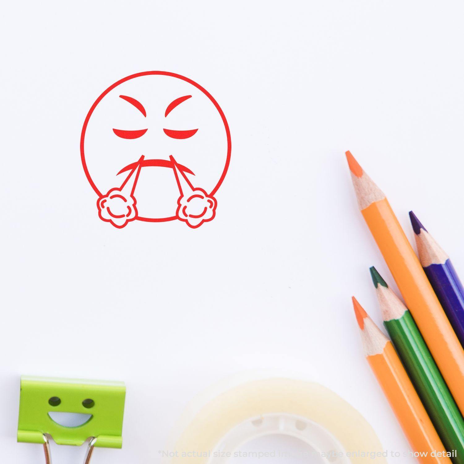 Round Angry Smiley Rubber Stamp in red ink on white paper, surrounded by colored pencils, tape, and a green binder clip.