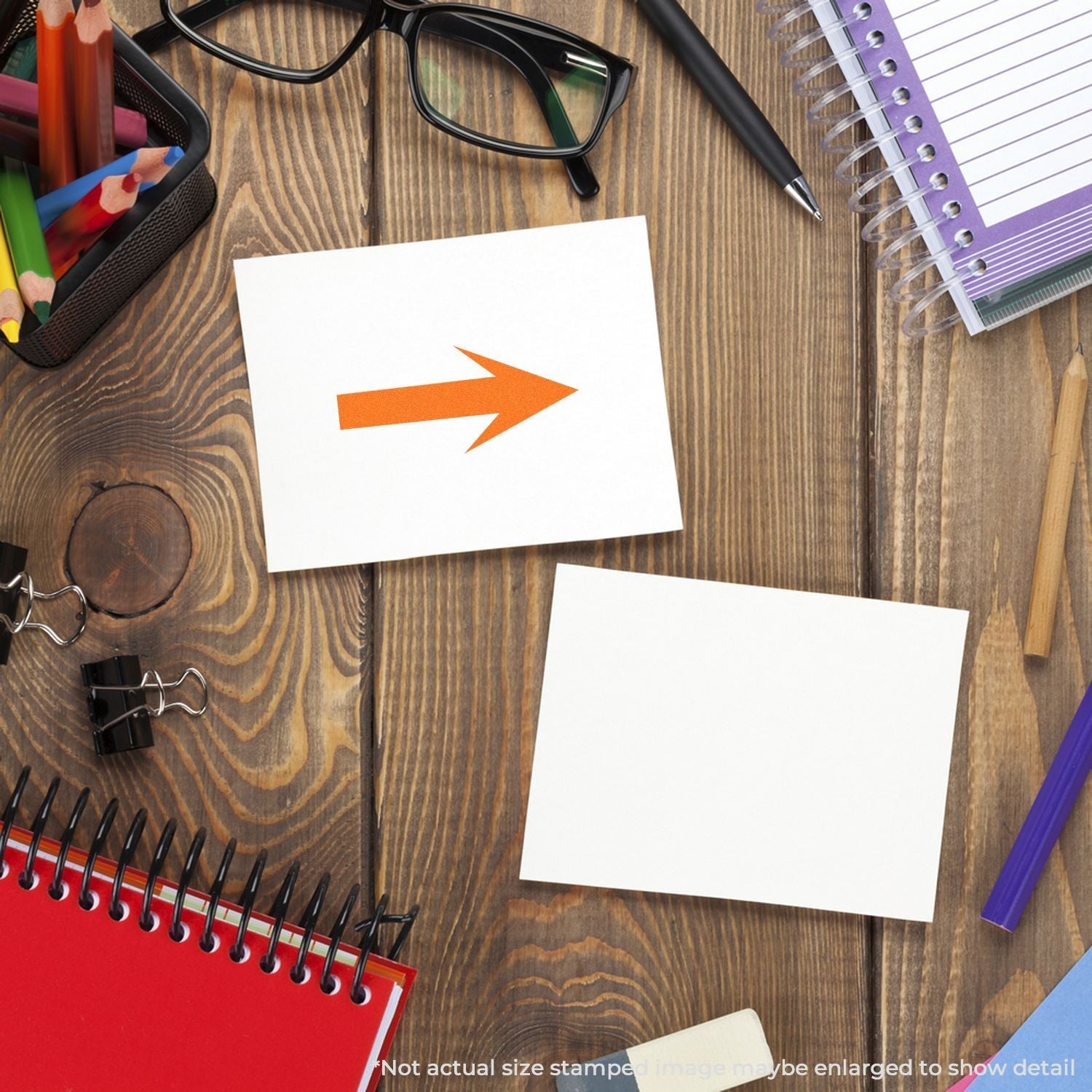 Self Inking Round Arrow Stamp on a wooden desk with stationery items, showing an orange arrow stamped on a white card.