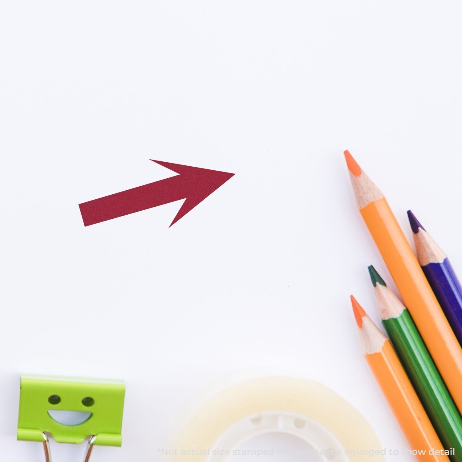 Self Inking Round Arrow Stamp imprint in red on white paper, surrounded by colorful pencils, a smiling binder clip, and a roll of tape.