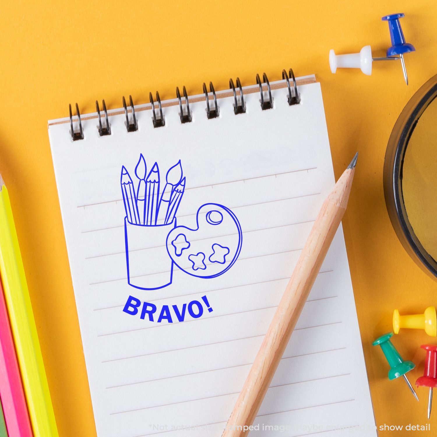 Self Inking Round Bravo Stamp on a notepad with a pencil, colored pens, and push pins on a yellow background.