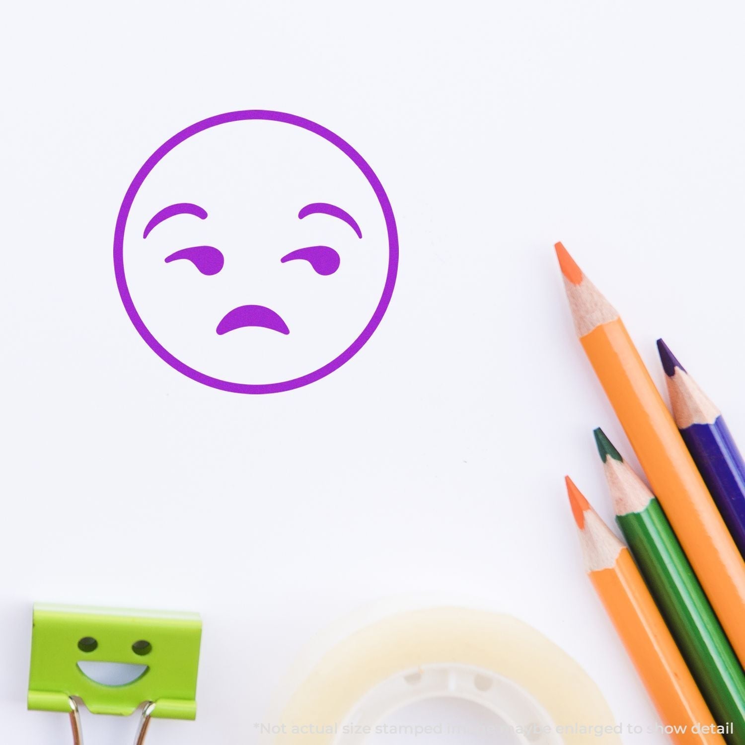 Self Inking Round Calm Smiley Stamp in purple ink on white paper, surrounded by colorful pencils, a green binder clip, and tape.