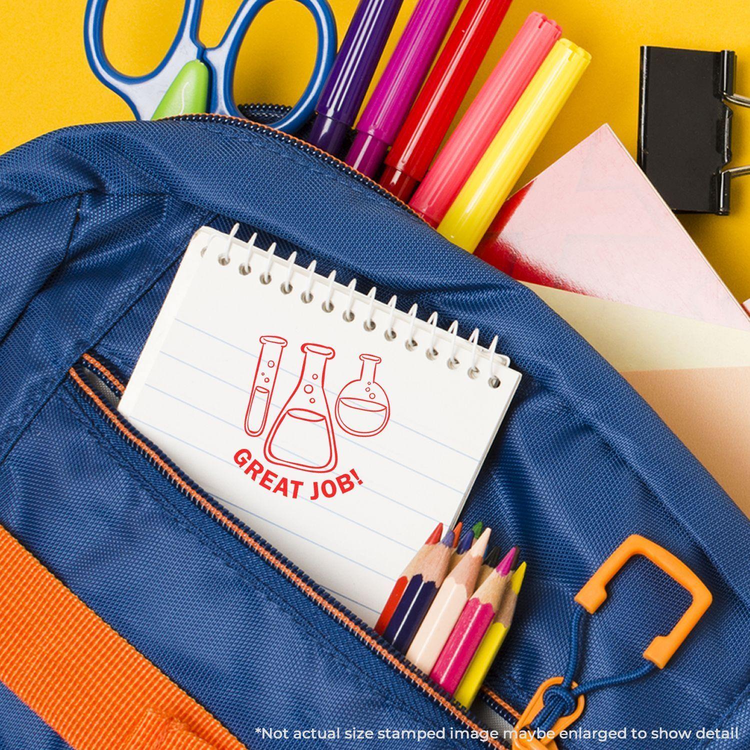 Round Chemistry Great Job rubber stamp on a notebook in a blue backpack with colorful pens, pencils, and school supplies.