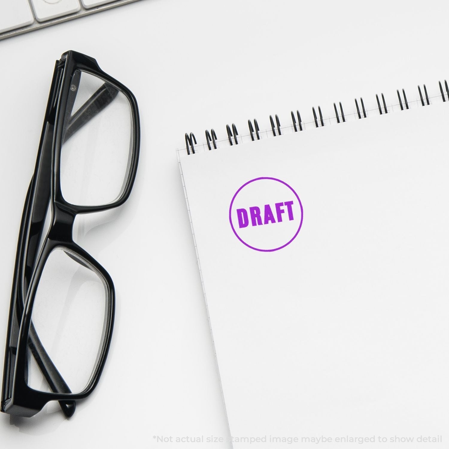 Self Inking Round Draft Stamp in purple ink on a white notepad, next to black glasses and a keyboard.