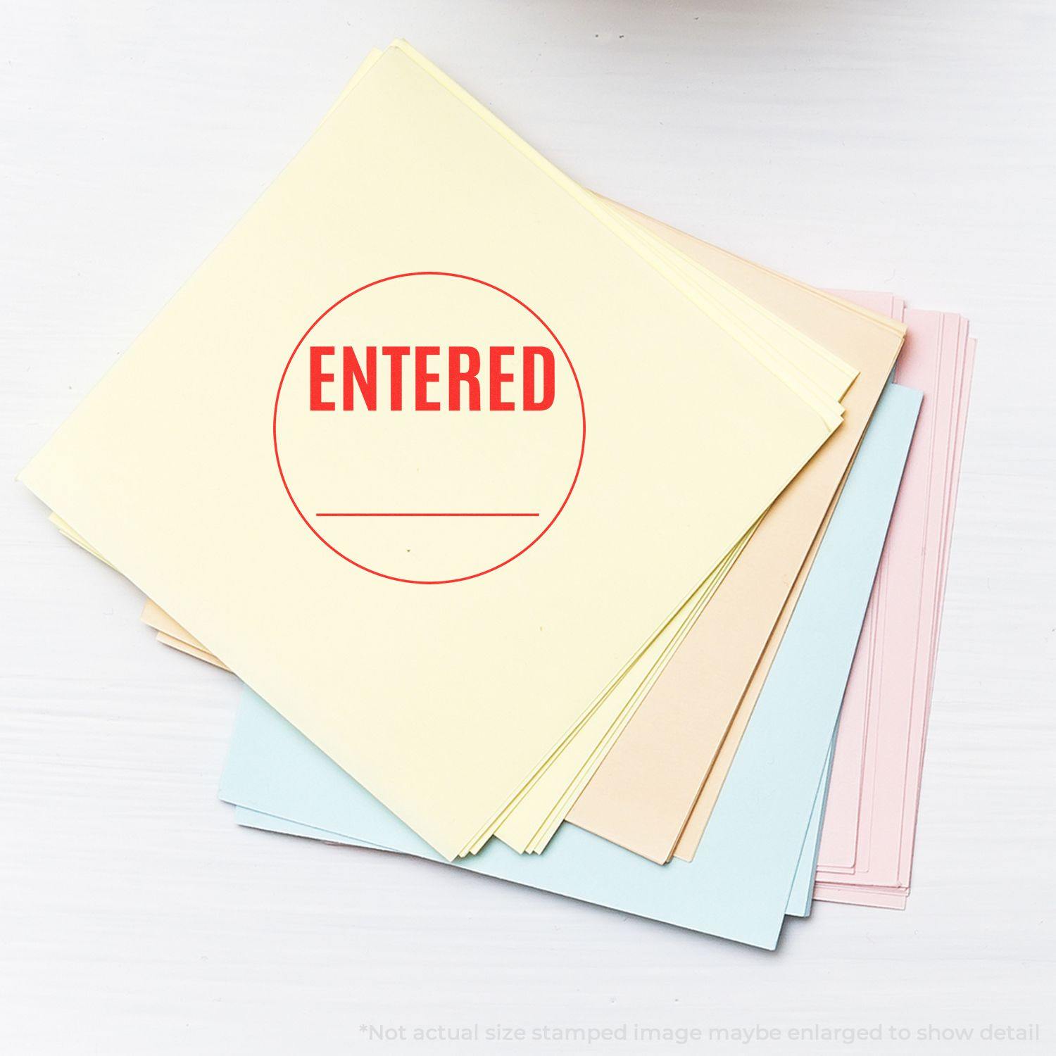 Round Entered rubber stamp in red ink on a stack of pastel-colored papers, with the word ENTERED prominently displayed in the center.