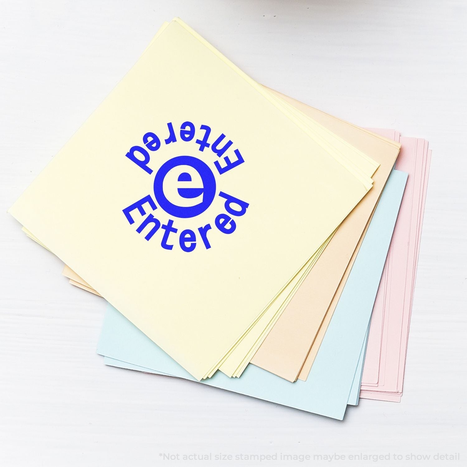 Self Inking Round Entered Entered Stamp in blue ink on a stack of pastel-colored papers.