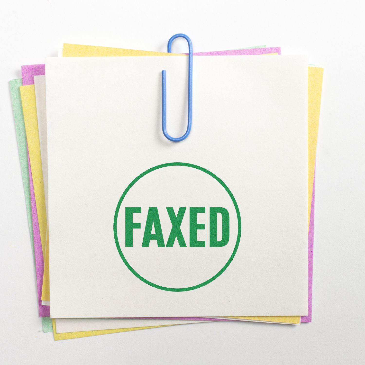 Round faxed rubber stamp in green ink on a stack of colorful papers held together by a blue paperclip.