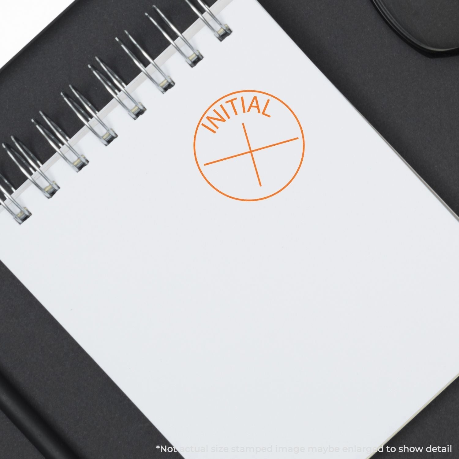 Self Inking Round Initial Stamp used on a white notepad, showing a clear orange INITIAL imprint with a cross in the center.