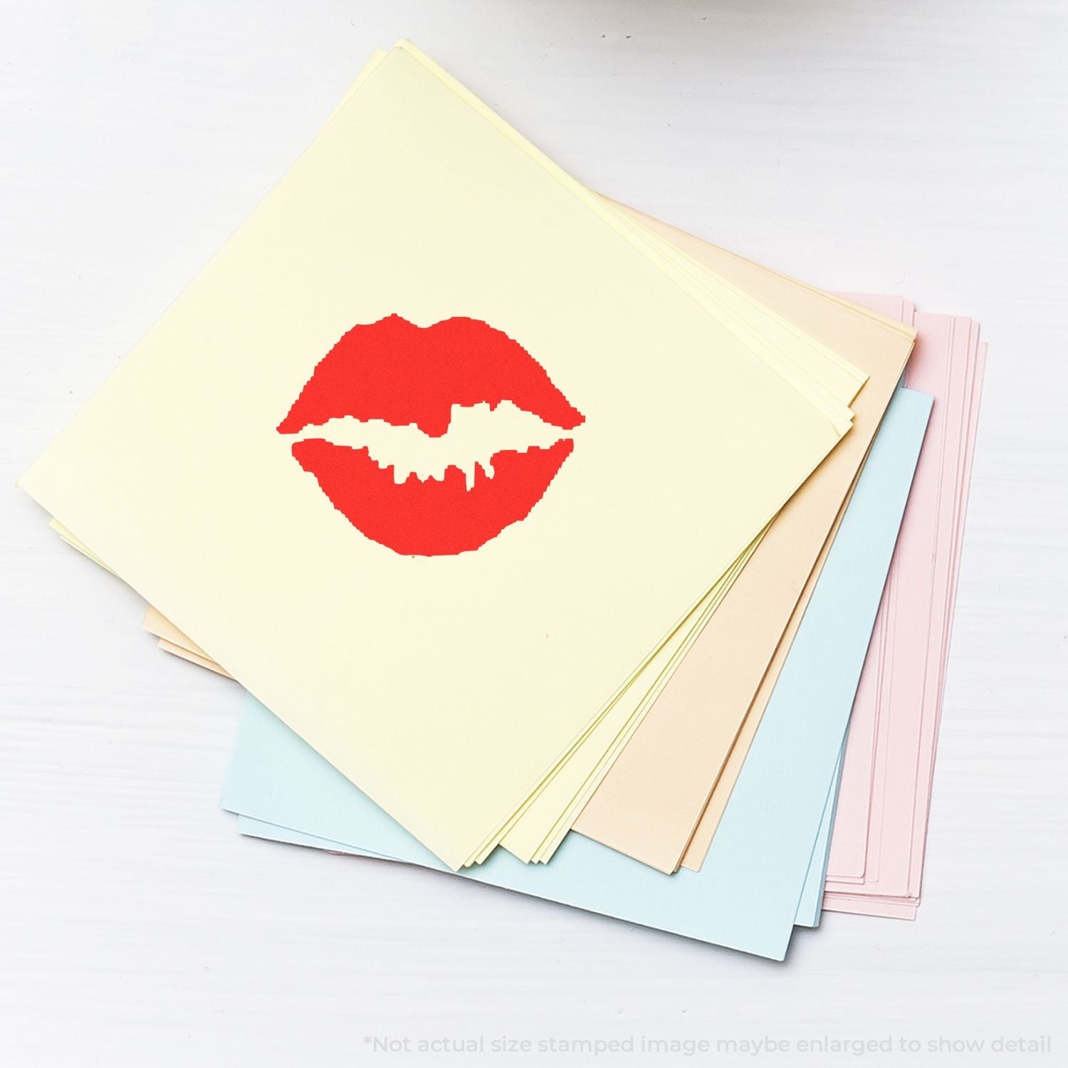 A stack of pastel papers with a red kiss mark from the Self Inking Round Kiss Stamp on top, placed on a white surface.